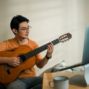 Man playing guitar on laptop computer. Teleconferencing music with his friend via video call on internet.