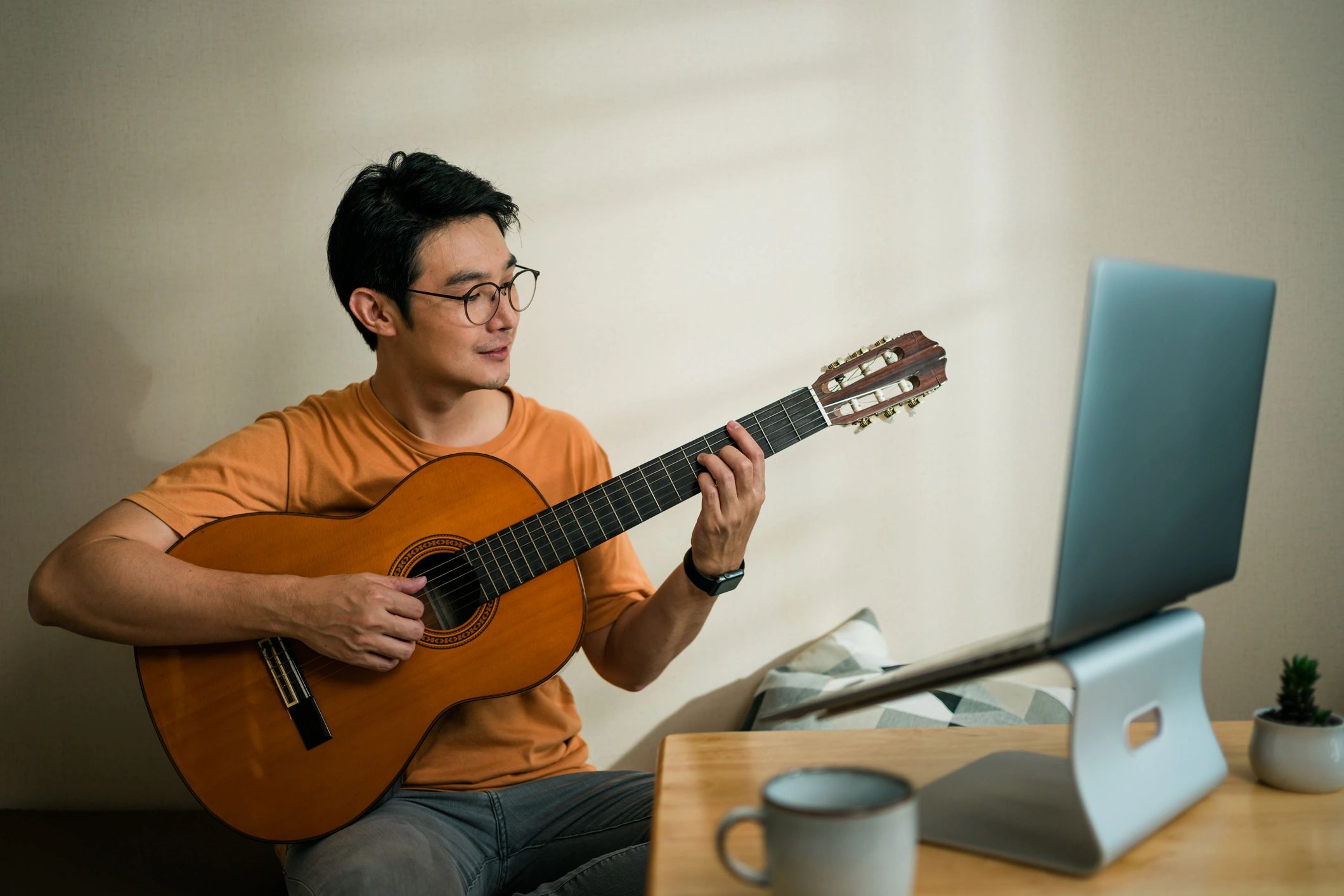 Man playing guitar on laptop computer. Teleconferencing music with his friend via video call on internet.
